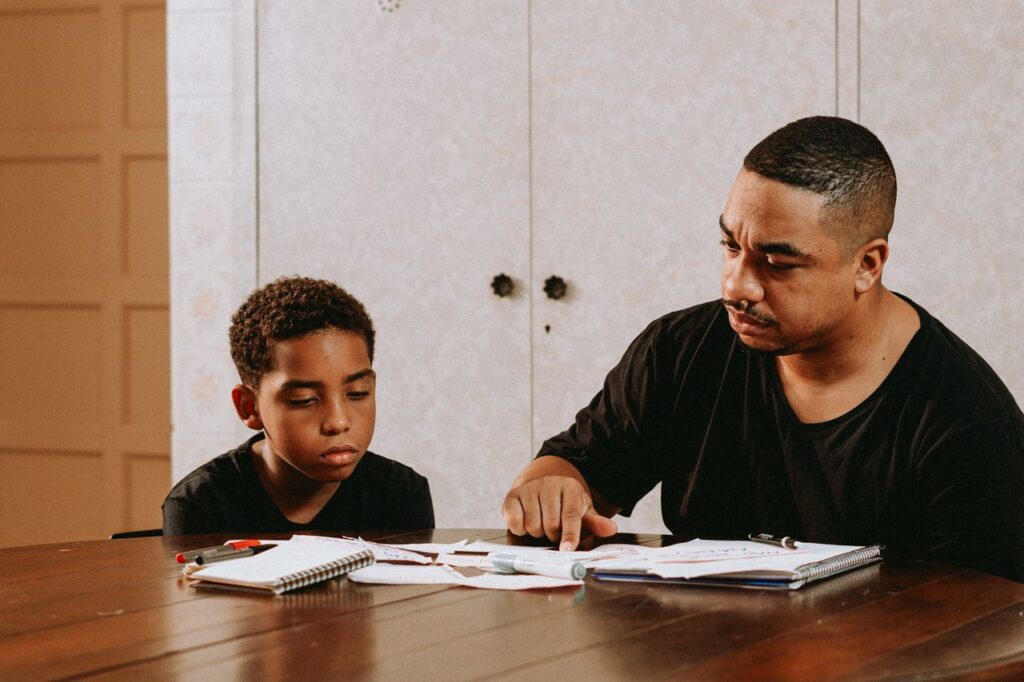 pexels-photo-27254264 A father helps his son with homework at a dining table, promoting learning and bonding.