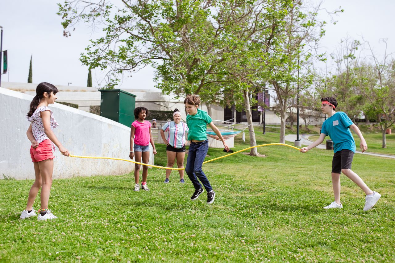 A group of diverse children joyfully playing jump rope outdoors in a sunny park.
