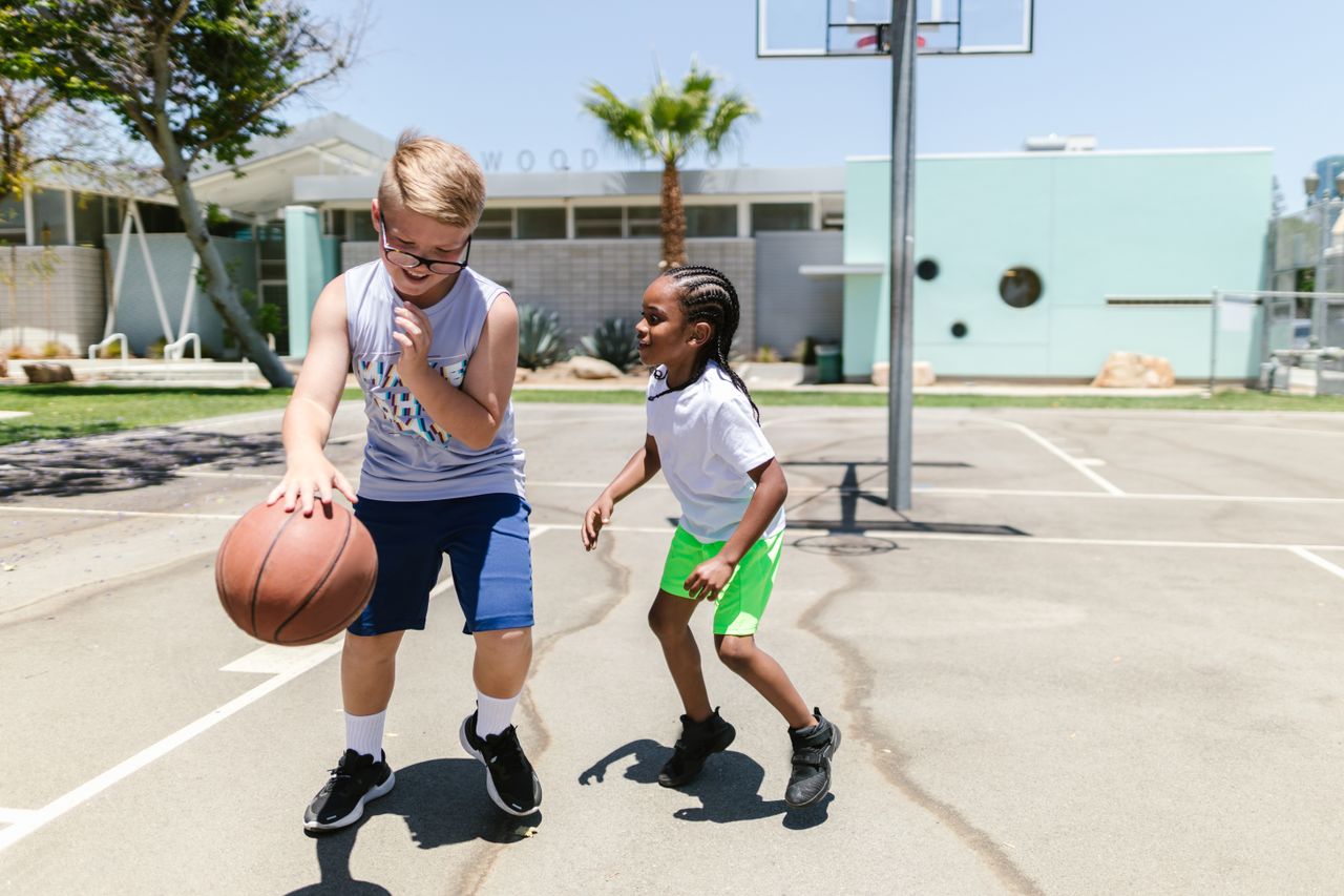 Two kids enjoying a game of basketball outdoors, showcasing fun and friendship.